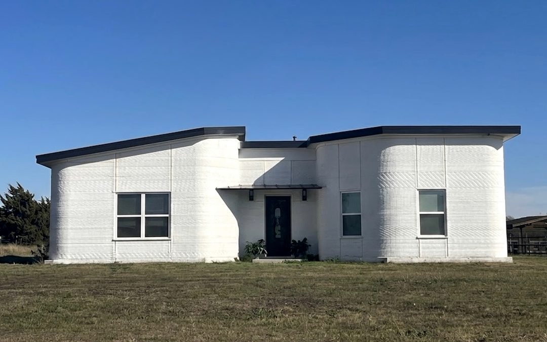 Completed 3D-printed concrete home with curved walls, flat roof, and front entry